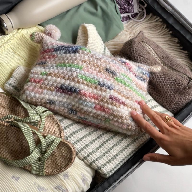 En person har pakket en kuffert til sin sommerferie. Forrest ligger en Shell clutch med strikkepinde osv. til rejsen.